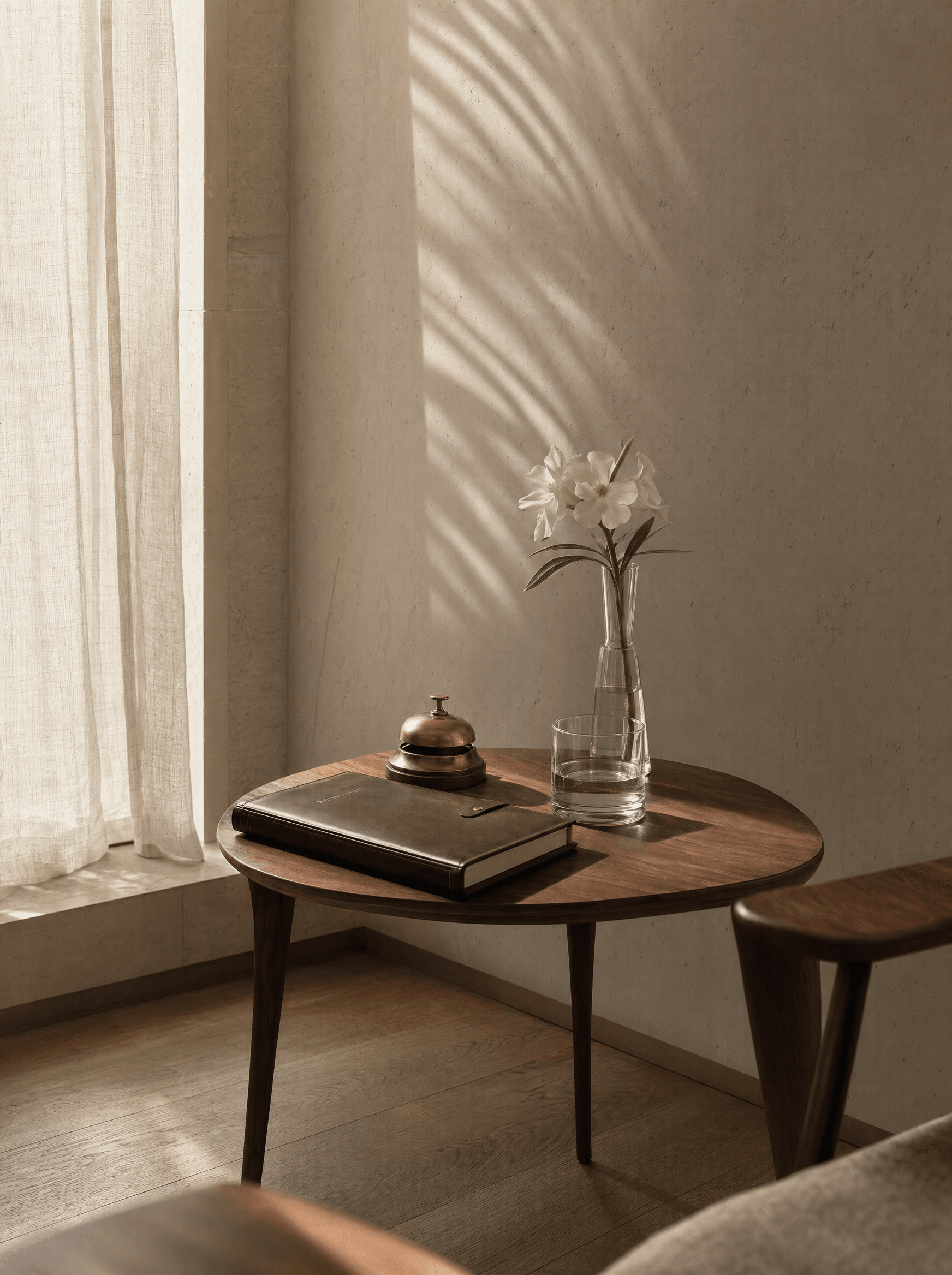 A private clinic side table at dawn — leather appointment book, brass desk bell, and a single white desert rose